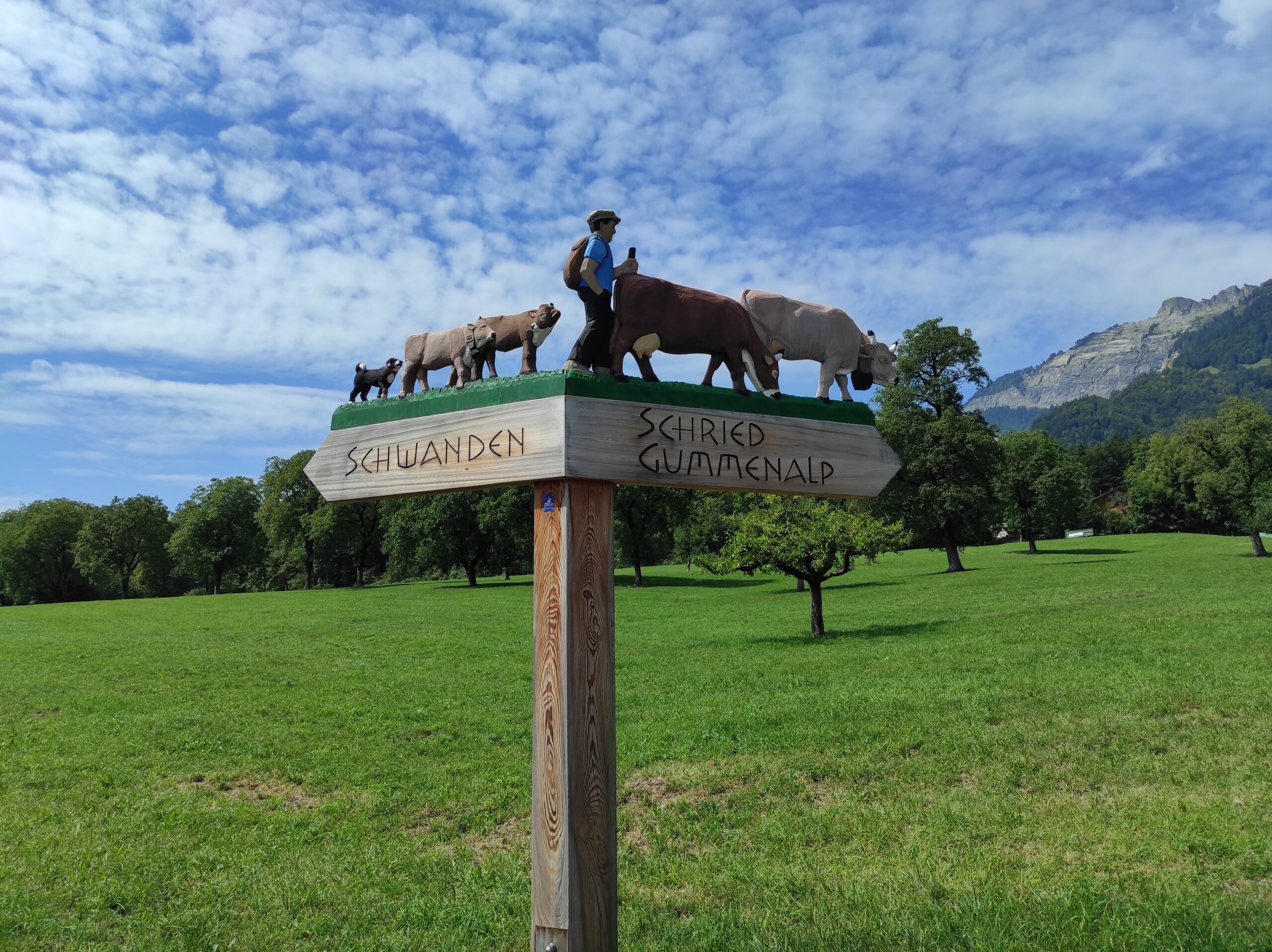 Wegweiser mit geschnitzten Holzfiguren nach Schwanden und Schried/Gummenalp